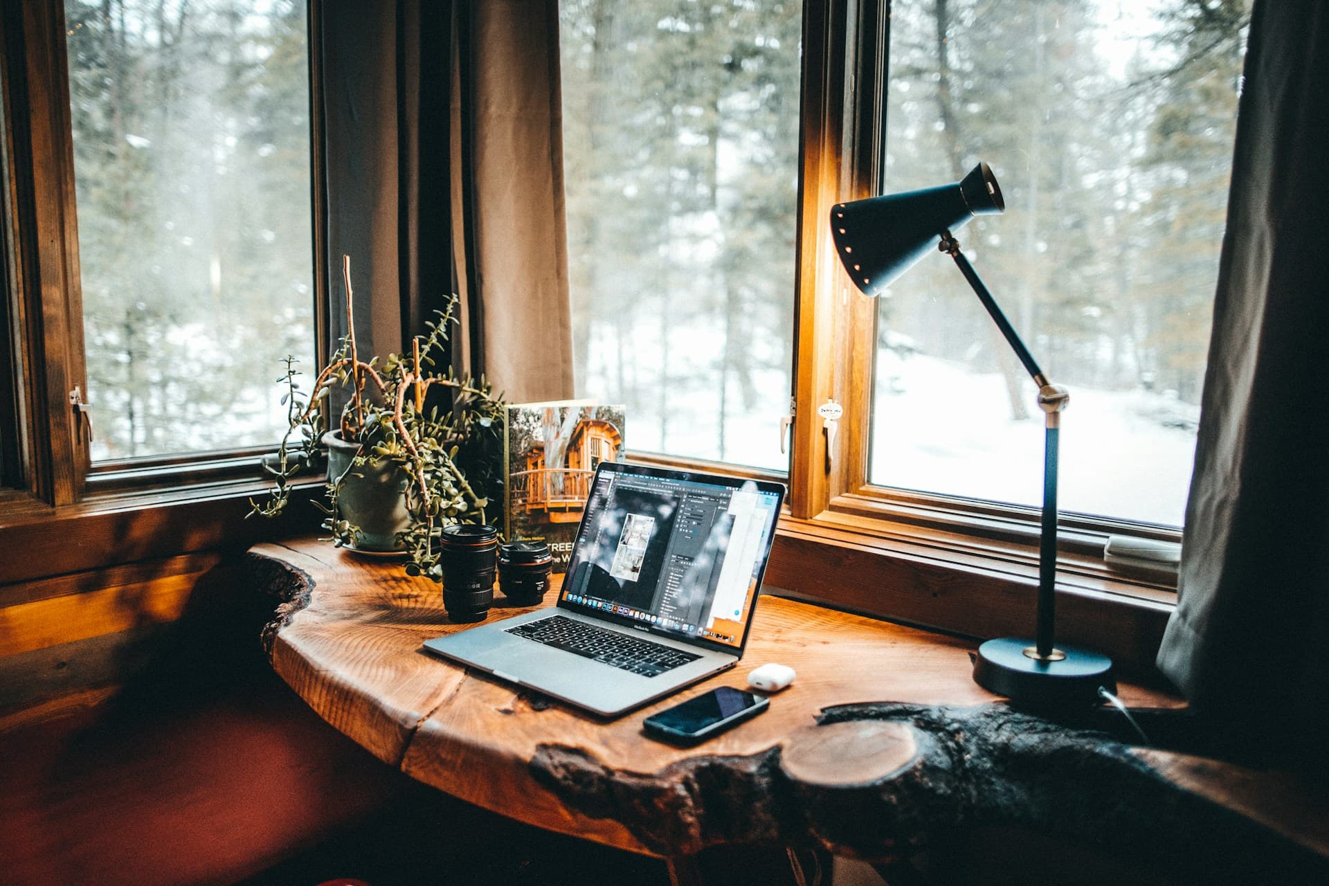 Designer-Workspace: MacBook auf Holzfenster, warme Schreibtischlampe, Wald im Hintergrund